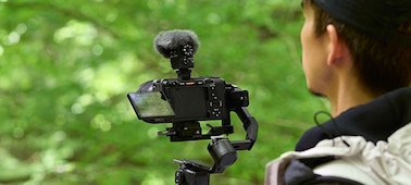 Usage image showing user shooting hand-held with microphone and wind screen attached to camera