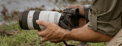 Example image showing a man holding camera in low position with LCD monitor flipped and angled for better visibility in a muddy field