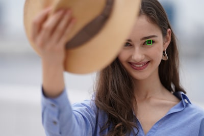 Image of a female model holding a hat that obscures part of her face, with an AF frame superimposed over one eye